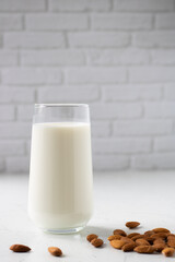 A glass of almond milk close-up next to scattered almonds nearby.