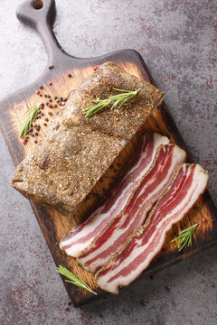 Smoked italian pancetta meat closeup on the wooden board on the table. Vertical top view from above