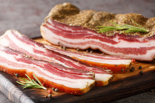 Dry-cured pork belly bacon with spices and rosemary close-up on a wooden board on the table. horizontal