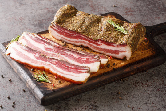 Pancetta Italian is a salt cured pork belly salume closeup on the wooden board on the table. Horizontal
