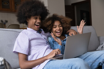 Happy overjoyed teen Black couple staring at laptop display, making winner hands, laughing, celebrating success, achieve, reward, getting good surprising news, feeling joy, euphoria