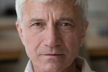 Close up portrait wrinkled face hoary senior man grandfather retiree posing indoors with unhappy serious look. Thoughtful grey haired old male pensioner stand at home look at camera ponder on problems