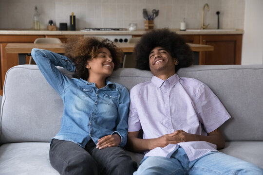Care free happy Black couple of teenagers enjoying leisure, relaxing on couch, breathing fresh air with closed eyes, laughing, talking. Teen African elder brother and sister home shot - Powered by Adobe