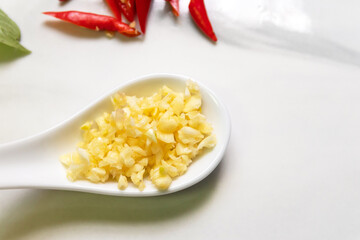 Chopped garlic in a spoon on white marble board, top view.