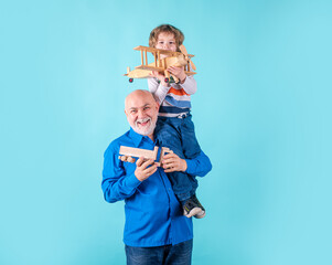 Grandfather and grandson piggyback with toy plane and wooden truck. Men generation granddad and...