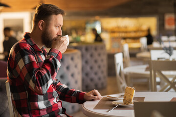 Pensive bearded guy enjoying morning coffee for breakfast looking away through window in cafeteria, caucasian male in casual outfit drinking beverage in cafe