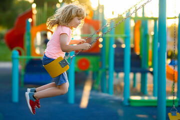 Kids play on school or kindergarten yard. Little boy having fun on a swing on the playground in...