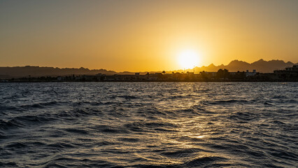 Sunset over the Red Sea. The sun is low over a picturesque mountain range. The sky is colored orange. Ripples and highlights on the water. Egypt. Safaga