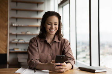 Obraz premium Happy female employee reading text message on cell screen, chatting online, shopping, making call, smiling. Businesswoman using smartphone with financial banking app, virtual service for payment