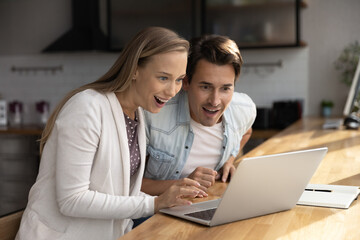 Happy surprised millennial couple using laptop, staring at screen, getting good awesome news, mortgage approval, winning prize, unexpected money, income, benefit, excited with discount, sale