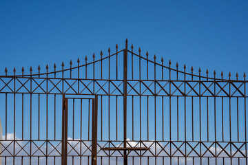an old rusty metal fence against a blue sky background, looks like a gate to heaven