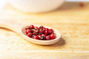 Red or pink peppercorns on wooden spoon.