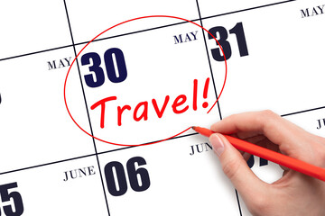 Hand drawing a red circle and writing the text TRAVEL on the calendar date 30 May. Travel planning.