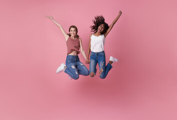 Two happy carefree young women jumping in the air with raised fists looking at camera isolated on...