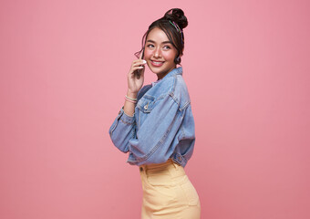 Happy young Asian teen woman talking mobile phone isolated on studio pink background.