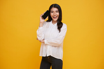 Happy young Asian woman showing at blank screen mobile phone isolated over yellow background.
