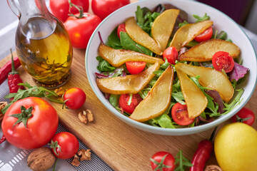 Salad with pears, tomatoes and arugula on wooden board