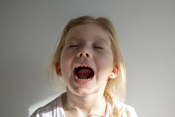 Screaming child girl with closed eyes on the background of a white wall.