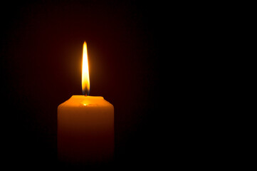 A single burning candle flame or light is glowing on a yellow candle on black or dark background on...