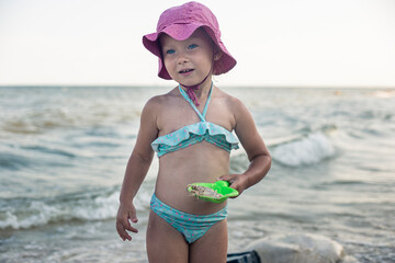 Little child girl in a swimsuit, in a Panama, plays near the sea.