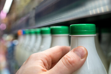 Buying milk in the store. Man's hand holding a bottle of milk in a supermarket.