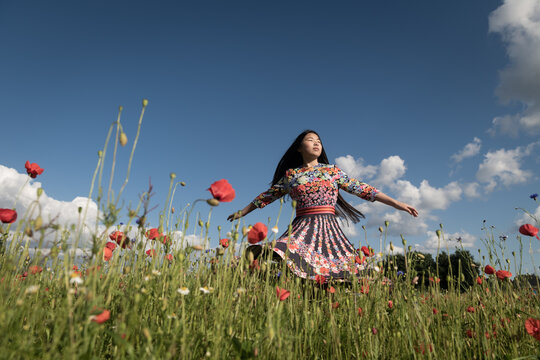 Happy girl dancing in floral dress in poppy field in summer