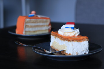 Two orange cakes/ pie slices. Tompouce and chipolata. With cream on top and a little red white blue flag. 