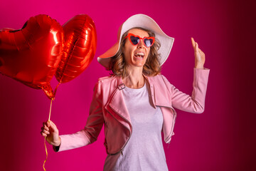 A caucasian woman enjoying dancing with a white hat in a nightclub with some heart balloons, pink background