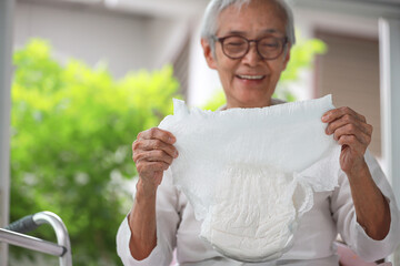Happy smiling asian senior woman showing disposable diaper for adult,looking at nappy pamper with satisfaction,old elderly patient with urinary incontinence,consumer goods,health care concept - obrazy, fototapety, plakaty
