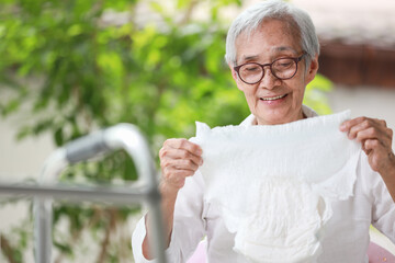 Happy smiling asian senior woman holding disposable diaper for adult,looking at nappy pamper with satisfaction,old elderly patient with urinary incontinence,consumer goods,health care concept