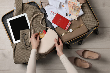 Woman packing suitcase for business trip on wooden floor, top view