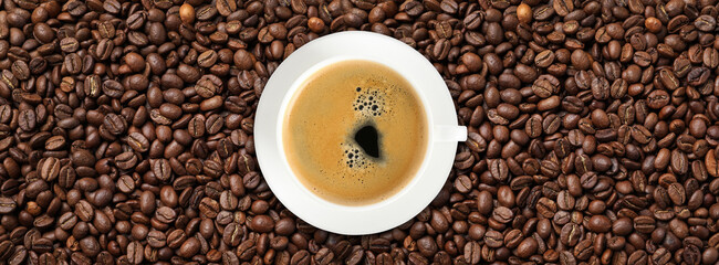 Cup of tasty aromatic coffee on roasted beans, top view. Banner design