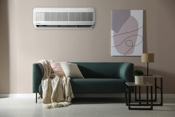 Modern air conditioner on beige wall in room with stylish sofa