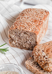 Sliced bread with sesame seeds on a light tablecloth with rosemary.