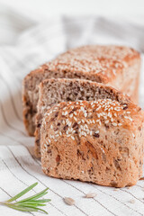 Sliced bread with sesame seeds on a light tablecloth with rosemary. Side view.