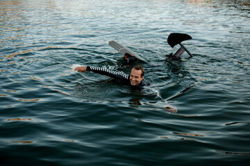 smiling man in wetsuit with a foil wakeboard swims in the water