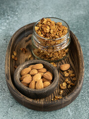 Granola in the glass jar on the wooden oval plate. Almonds in the small wooden bowl. Healthy...