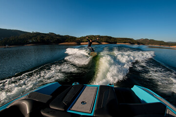 view from boat on man masterfully jumping with wakesurf board on a wave