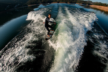 high angle view of young athletic man skillfully balancing on a wave on a wakesurf board