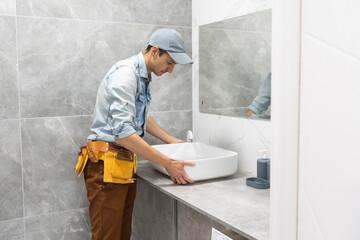 Professional plumber, male worker in uniform installing sink and water pipe in new apartment