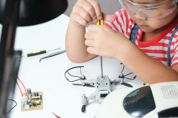 Concentrated little girl repairing her toy drone with a tool in hand and carefully assembles toy drone with screwdriver. STEM Hobbies for advanced smart kids.