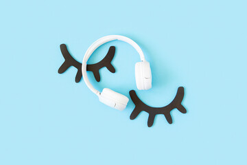 Eyelashes and white headphones on blue background. Concept Sleep learning, audiobook or lullaby for the night. Top view Flat lay