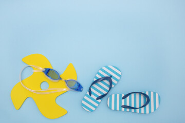 set of items for the beach - a toy, swimming goggles, children's flip flops on blue background with copy space, summer holidays.