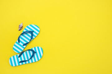 children's beach flip-flops and a seashell on a yellow background with copy space
