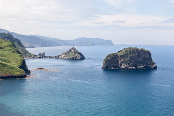 View from Matxitxako lighthouse to 2 little rocky islands Gaztelugatxe and Aketx and part of green coastline with shallow waters of Bay of Biscay, Basque Country, Spain