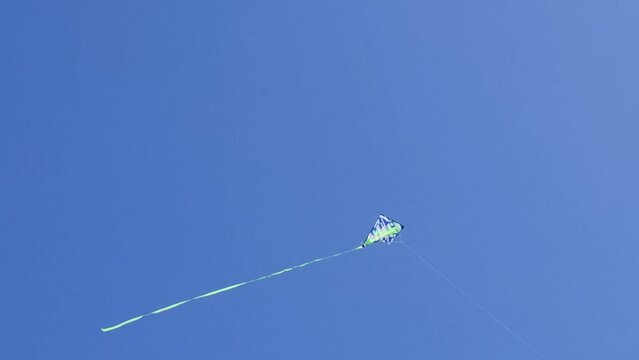 A bright kite with a long tail made of silk ribbons flies in a light wind against a blue sky in the rays of the sun during the day. Symbol of freedom and childhood. The concept of freedom, summer hobb