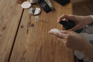 From above of crop woman applying moisturizing facial toner or micellar water on cotton pad while...