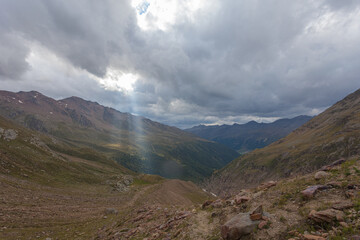 Fototapeta premium Bright sunlight shining through hole of clouds to alpine scene of mountain range and valley before sunset. Vallelunga, Alto Adige Sudtirol, Italy