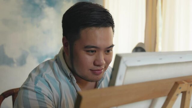 Portrait of a chubby Asian young man happy creating front of canvas