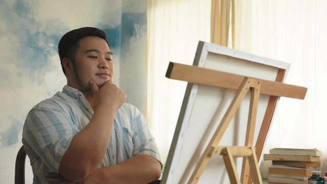 Portrait of a chubby Asian young man happy creating front of canvas